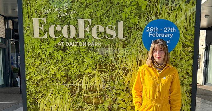 blogger Tasha Steel smiling at camera in front of green sign for Ecofest at Dalton Park
